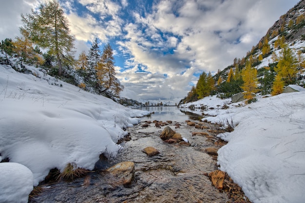 Il piccolo fiume di montagna entra nel lago in autunno con la prima neve