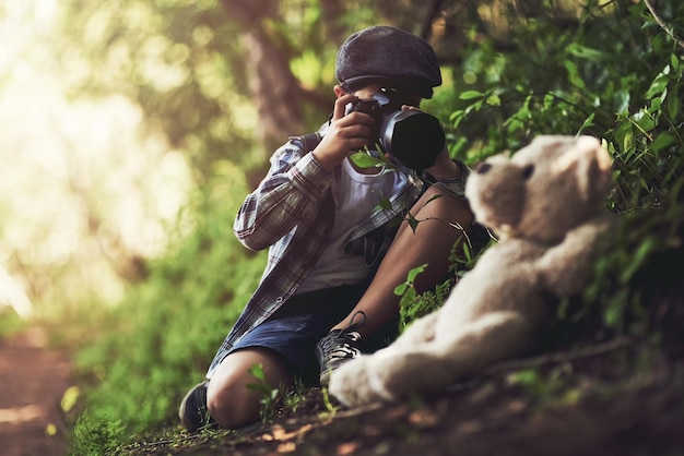 È il piccolo fotografo più carino Scatto di un ragazzo non identificabile che usa una fotocamera per scattare foto del suo orsacchiotto nel bosco