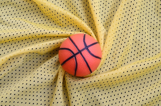 Il piccolo pallacanestro di gomma arancione si trova su una maglia sportiva gialla