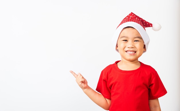 Il piccolo ragazzo asiatico carino sorride ed emozionato Bambini vestiti con il cappello rosso di Babbo Natale puntano il dito