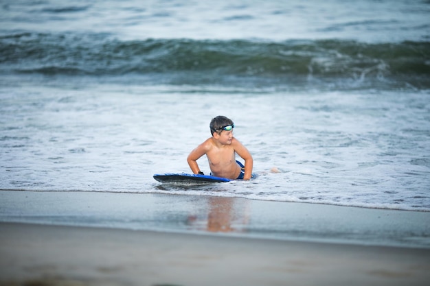 Il piccolo surfista impara a cavalcare la tavola da surf sull'onda del mare Il ragazzo gioca in estate imparando il surf nell'oceano Il ragazzino nuota sulla tavola da surf