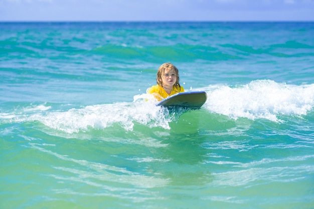 Il piccolo surfista impara a cavalcare sulla tavola da surf sull'onda del mare, il bambino gioca in estate, la ragazza del mare sta imparando il sur