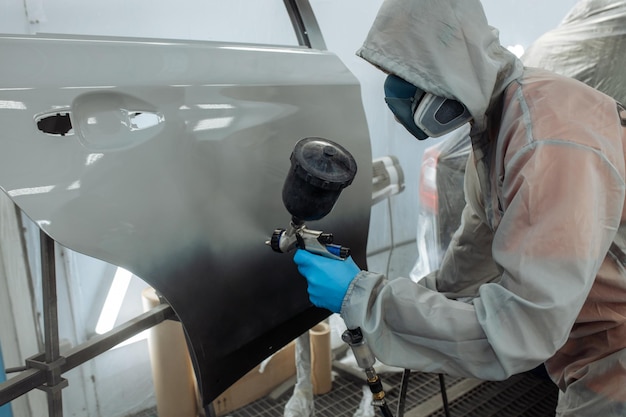 Il pittore di auto professionista sta dipingendo in garage con l'aerografo.