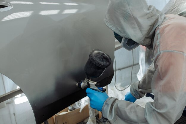 Il pittore di auto professionista sta dipingendo in garage con l'aerografo.