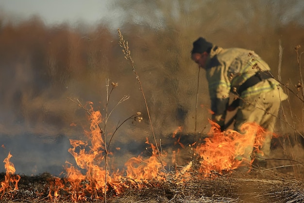 il pompiere spegne l'erba/incendio boschivo, l'erba secca brucia, il vento soffia