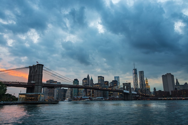 Il ponte di Brooklyn e lo skyline di New York attraverso l'East River al crepuscolo in una piovosa giornata estiva