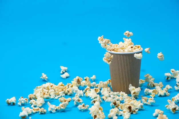 Il popcorn viene versato in un bicchiere di carta marrone su sfondo blu