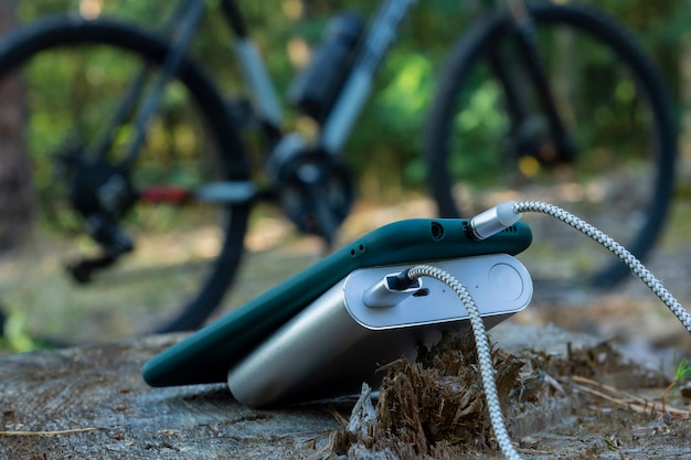 Il power bank carica uno smartphone nella foresta sullo sfondo di una bicicletta.