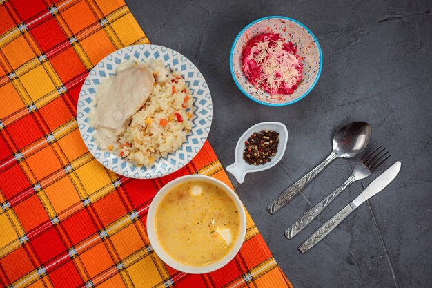 Il pranzo delizioso ha messo sulla tavola grigia coperta di asciugamano arancio. Il pranzo contiene zuppa, riso e pollo e salat di barbabietola.