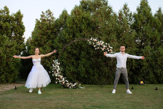 Il primo ballo dello sposo e della sposa in abito da sposa corto su un prato verde