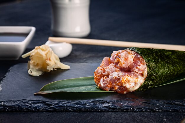 Il primo piano dei sushi saporiti del rotolo della mano con il caviale di tonno e di Tobico è servito sul piatto di pietra scuro con salsa di soia e zenzero