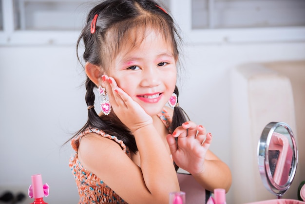 Il primo piano del bambino felice è una bella faccia truccata con un giocattolo di cosmetici