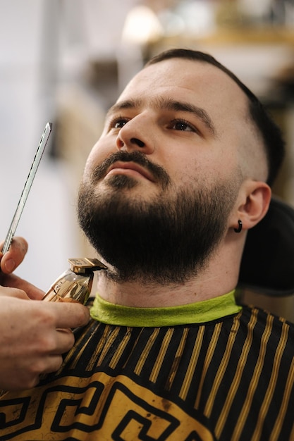 Il primo piano del barbiere professionista taglia al cliente la sua barba bell'uomo barbuto nel negozio di barbiere