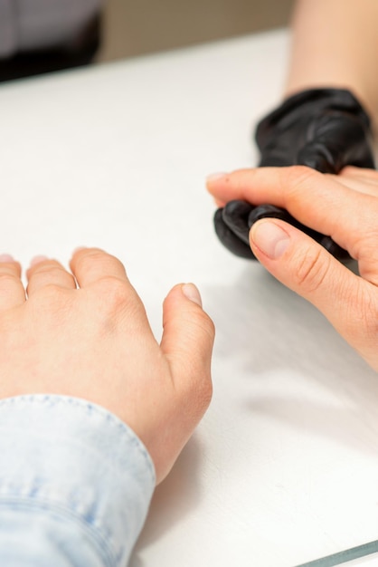 Il primo piano del maestro di manicure prepara le mani di una giovane donna per le procedure di manicure.