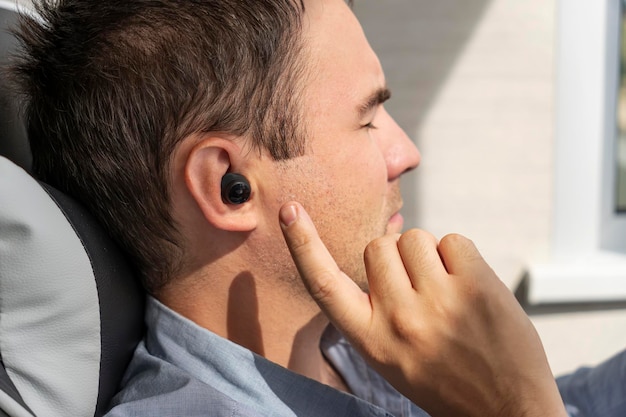 Il primo piano dell'auricolare wireless nell'orecchio umano inserisce l'auricolare nell'orecchio ascoltando musica con le cuffie