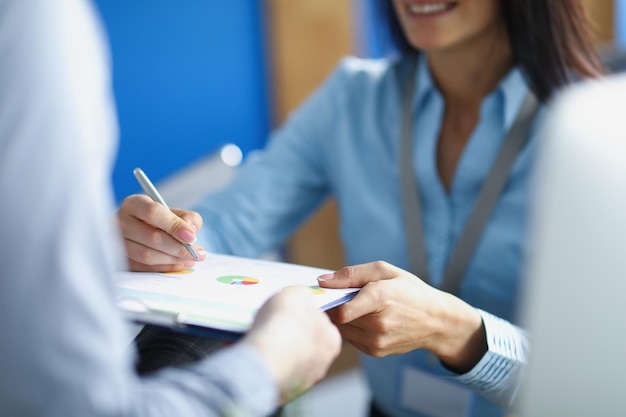 Il primo piano della lavoratrice esegue la correzione su carta da visita con la penna. La signora in tuta esprime l'idea al collega. Business, piano, creativo, concetto di strategia