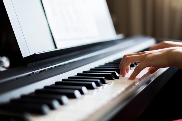 Il primo piano della mano di un esecutore di musica classica che gioca il piano o il sintetizzatore elettronico (tastiera di piano) ha offuscato il fondo