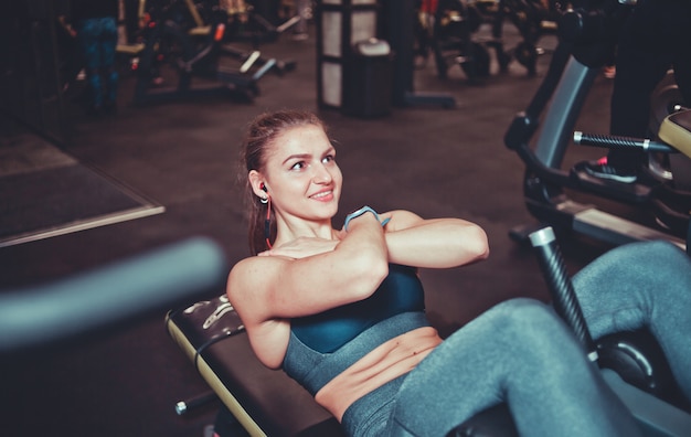 Il primo piano della ragazza atletica sorridente in abiti sportivi che fanno la flessione si esercita sui muscoli addominali