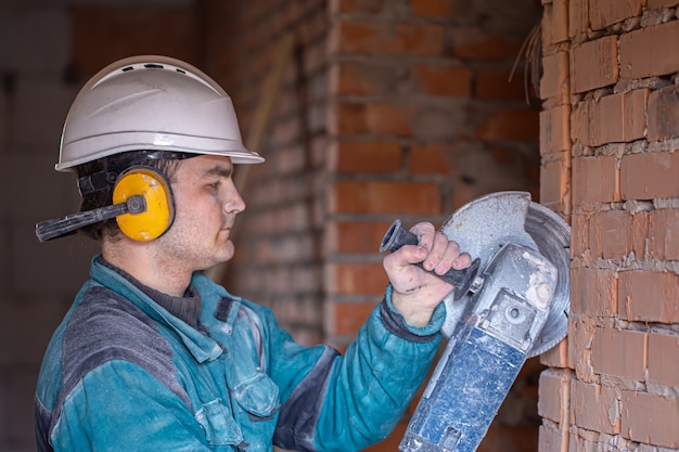 Il primo piano di un costruttore in un casco protettivo in una struttura di lavoro funziona con un utensile da taglio.