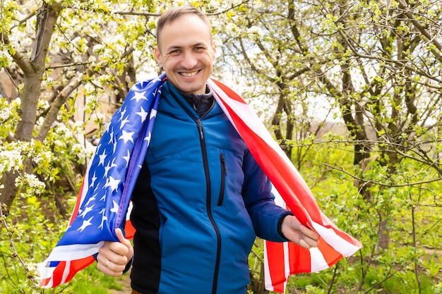 Il primo piano di un giovane agricoltore patriottico si erge tra il nuovo raccolto. Ragazzo che cammina con la bandiera americana sul campo di grano verde che celebra il giorno dell'indipendenza nazionale. 4 luglio concetto.