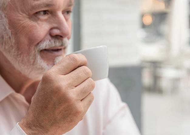 Il primo piano di un uomo più anziano sfocato che tiene una tazza di caffè o di tè