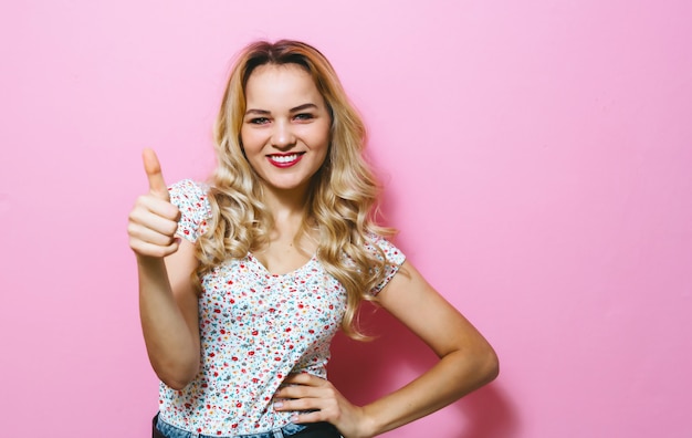 Il primo piano di una bionda presenta i gesti sopra la parete rosa