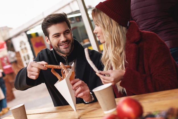 Il primo piano di una giovane coppia sta mangiando churros al mercato del cibo di strada