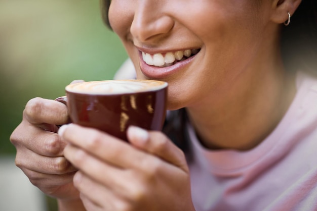 Il primo piano felice e la donna si rilassano con il contenuto del caffè e sono soddisfatti su uno sfondo sfocato Sorriso zoom e mani della ragazza con il tè al caffè all'aperto tranquillo e calmo mentre si gode la giornata o il fine settimana