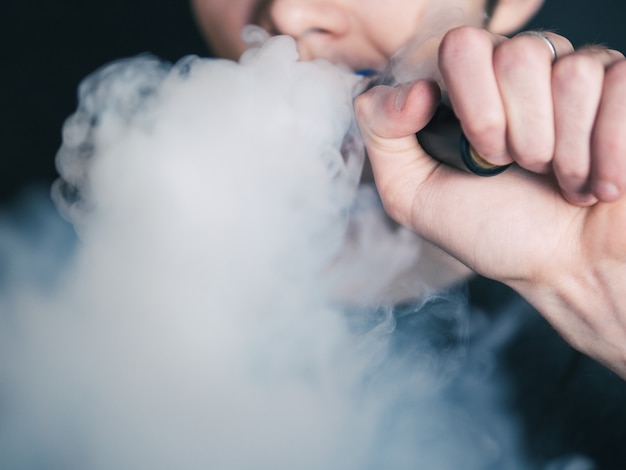 Il primo piano vaping dell'uomo espira il vapore