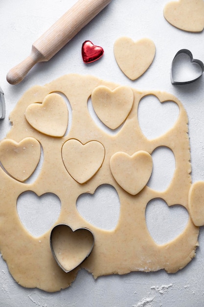 Il processo di cottura dei biscotti del cuore Vista dall'alto di pasta cruda mattarello e taglierine Immagine verticale