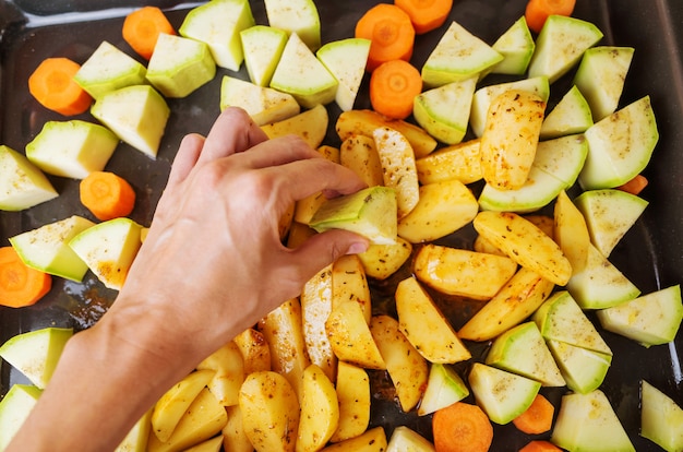 Il processo di cottura delle verdure al forno. Sulla teglia sono affettati zucchine, carote e patate.