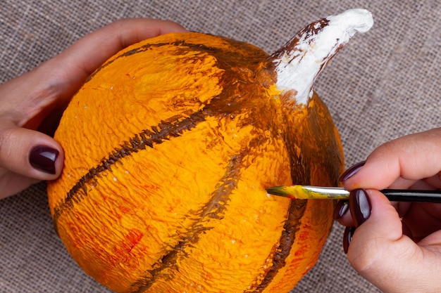 Il processo di creazione di una zucca in cartapesta per decorazioni di Halloween, disegno con colori, mani che tengono un pennello.