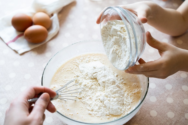 Il processo di preparazione della pasta per frittelle con ingredienti su un tavolo luminoso, uova e farina viene montato con un mixer