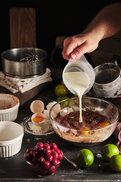 Il processo di preparazione della torta al cioccolato con ciliegie Prodotti per dessert su un tavolo da cucina in legno