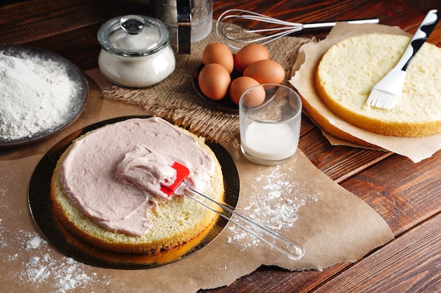 Il processo di preparazione della torta fatta in casa Crema di fragole rosa spalmata su uno strato Pan di Spagna biscotto da fare a casa Foto di alta qualità