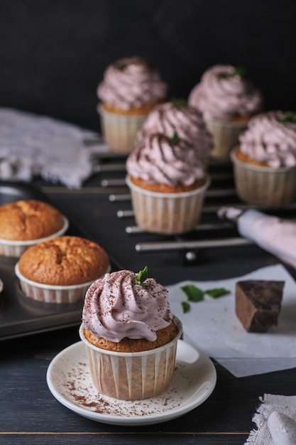Il processo di preparazione di cupcakes natalizi con crema rosa. Il dessert è decorato con foglie di menta e gocce di cioccolato.
