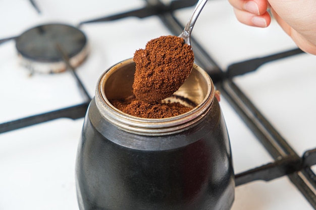 Il processo di versamento del caffè macinato fresco in una caffettiera geyser in piedi su un fornello a gas