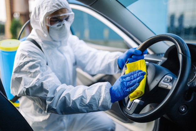 Il professionista della disinfezione pulisce il volante di un'auto