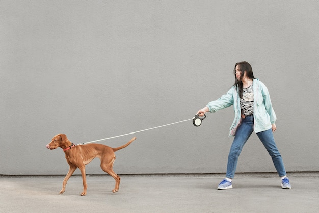 Il proprietario della donna porta un simpatico cane al guinzaglio sullo sfondo di un muro grigio.