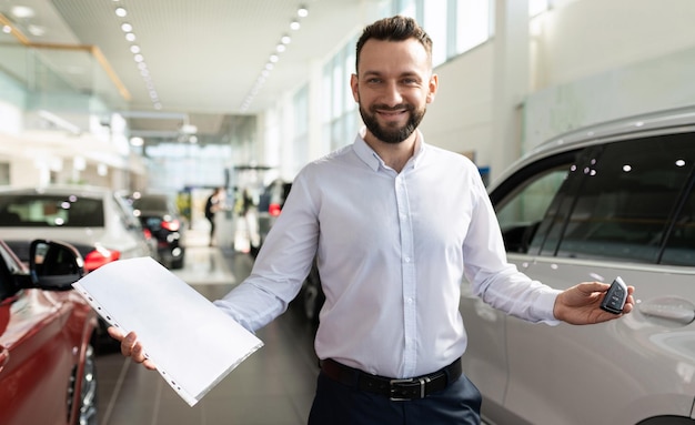 Il proprietario di un'auto nuova in uno showroom di un concessionario mostra documenti e chiavi di un'auto nuova