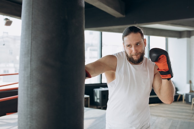 Il pugile colpisce il sacco da boxe in palestra al rallentatore. Giovane uomo allenamento al chiuso.