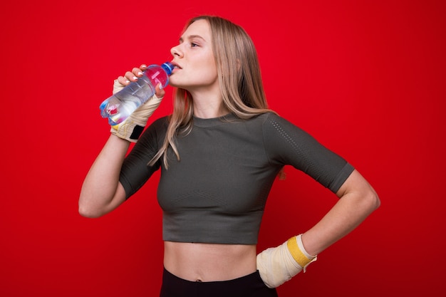 Il pugile femminile atletico beve l'acqua su fondo rosso