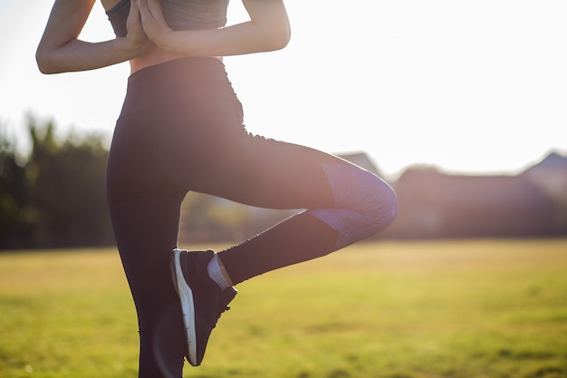 Il punto di vista posteriore della ragazza nella posizione di yoga medita nel campo all'alba.