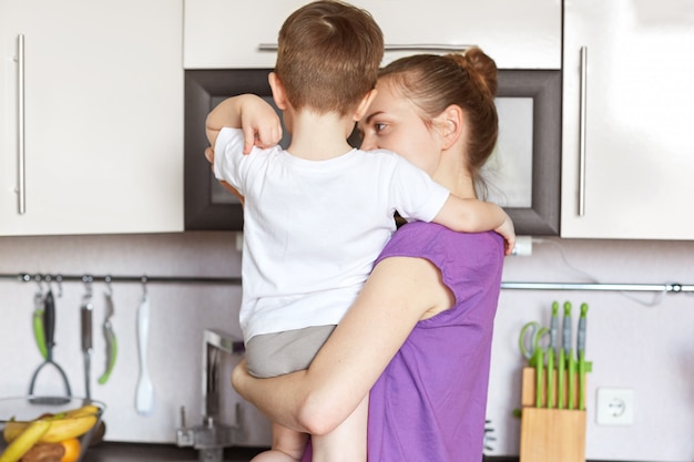 Il punto di vista posteriore di giovane madre esile tiene il figlio sulle mani