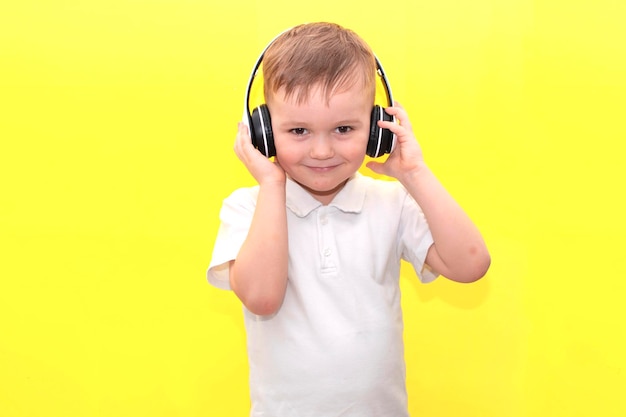 Il ragazzino ascolta musica con le cuffie su sfondo giallo. Il bambino carino gode di musica da ballo felice, sorride, posa contro il muro dello studio. di buon umore.