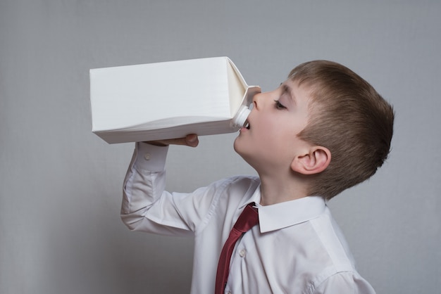 Il ragazzino beve da un grande pacchetto bianco.