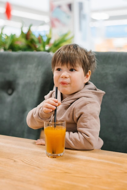 Il ragazzino beve il succo da una cannuccia mentre è seduto a un tavolo in un caffè Al bambino non piace una bevanda appena spremuta