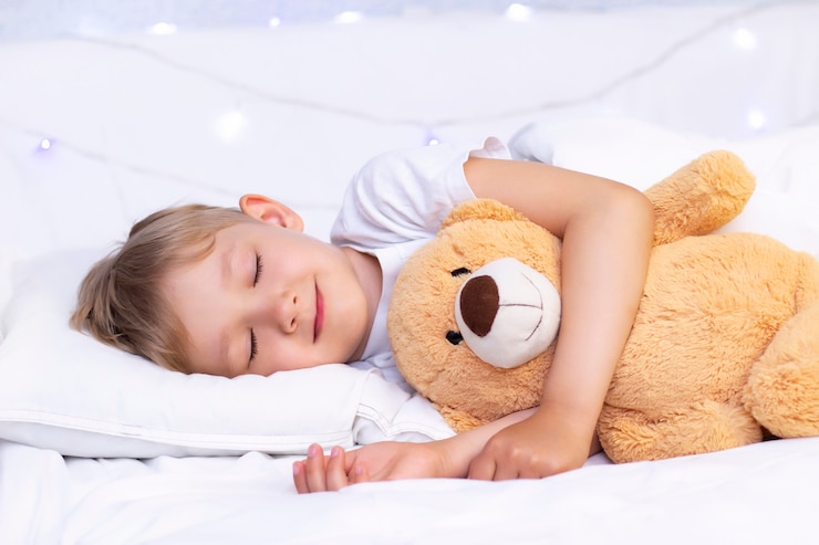 Il ragazzino bianco affascinante dorme a letto. abbraccia un peluche