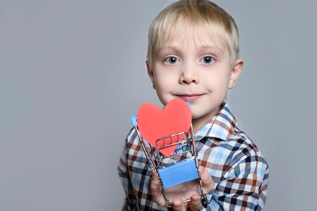 Il ragazzino biondo che tiene un carrello della spesa del metallo con un cuore ha modellato la cartolina dentro