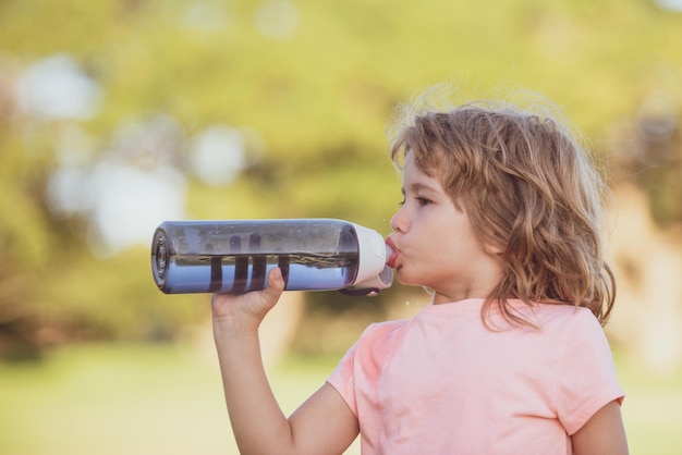 Il ragazzino carino beve acqua dalla bottiglia sportiva nel parco verde Closeup ritratto di bambino sportivo che si esercita all'aperto